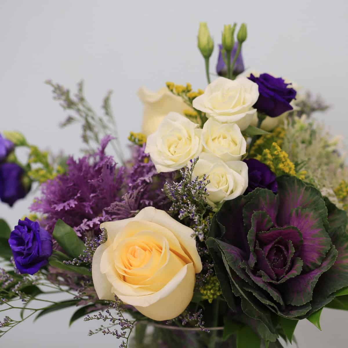 Close-up of Violet Embrace featuring white roses, purple lisianthus and decorative kale in signature Le Bouquet vase.