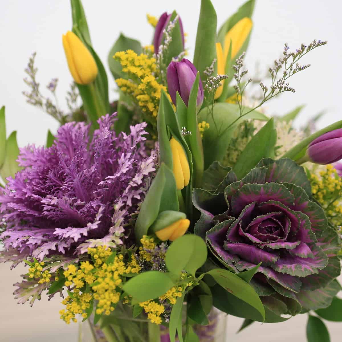 Close-up of Violet Embrace with purple and yellow tulips, decorative kale and textured greenery.