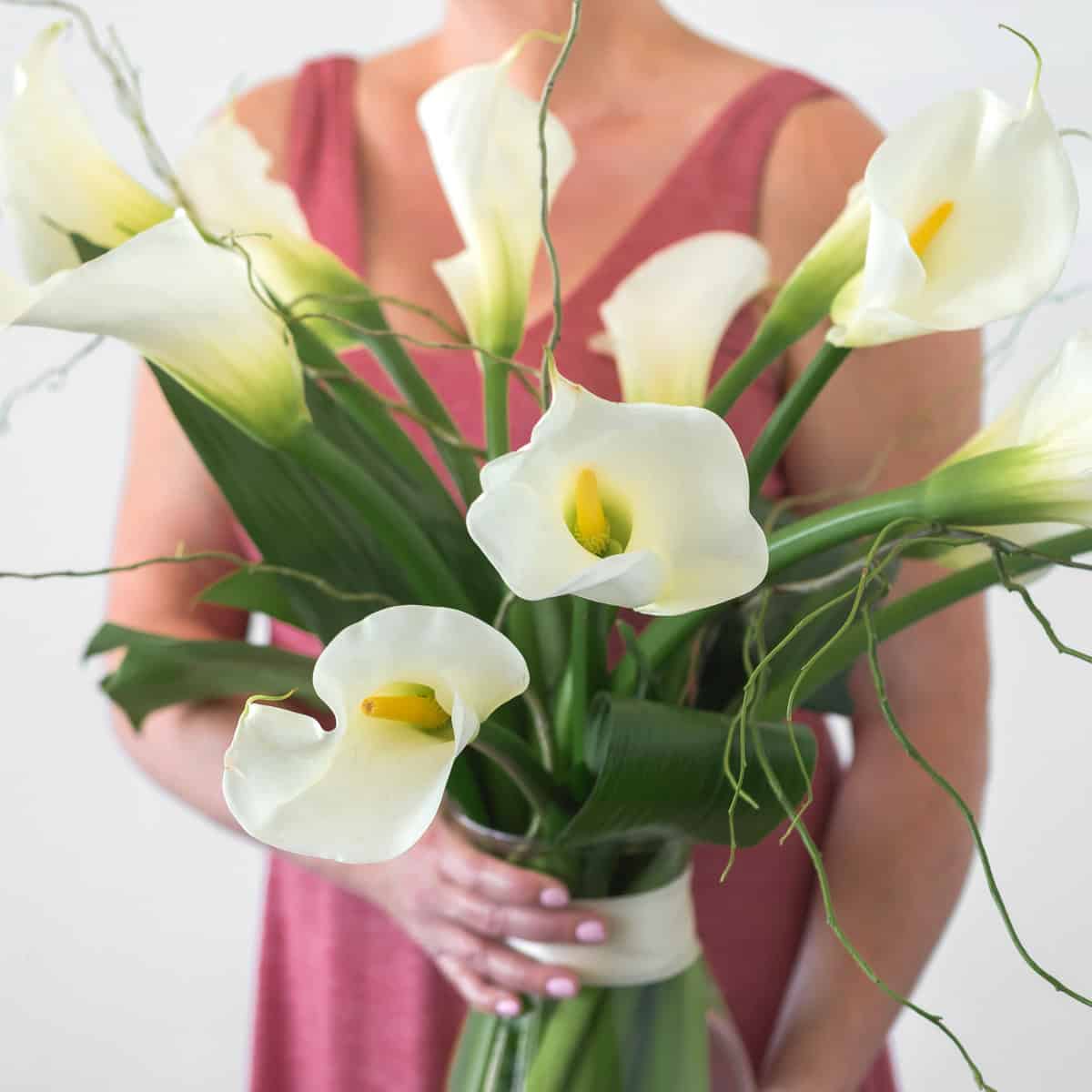 Person holding elegant white calla lily arrangement
