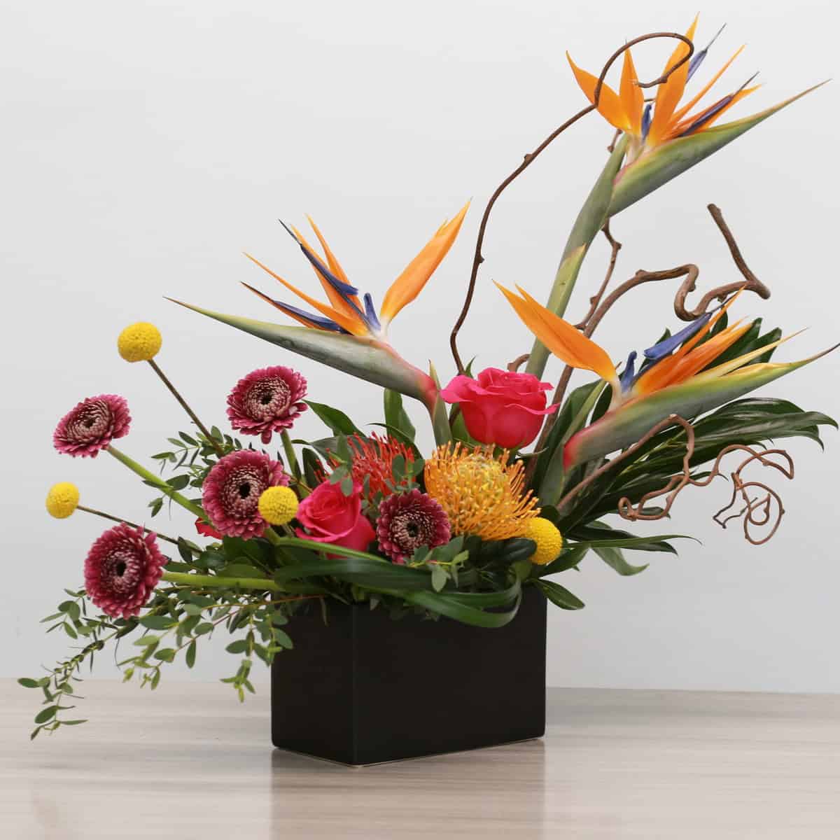 Angled view of Mango Fusion tropical arrangement with exotic flowers including birds of paradise and protea