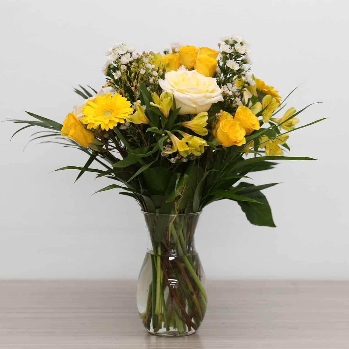 Golden Hour bouquet arranged in a glass vase with white roses, yellow flowers, and tropical greenery.