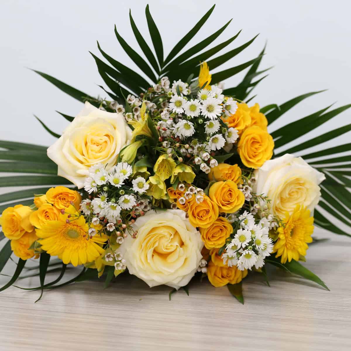 Wrapped Golden Hour bouquet with white roses, yellow gerberas, spray roses, and tropical foliage.