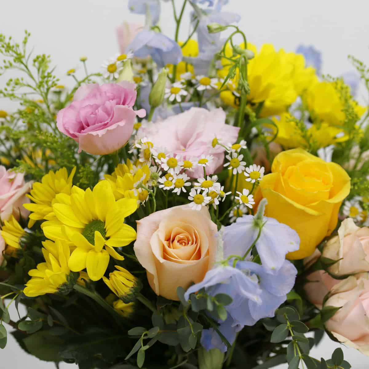 Close-up of Summer Morning bouquet featuring chamomile flowers, peach roses, pink lisianthus, and blue delphiniums.