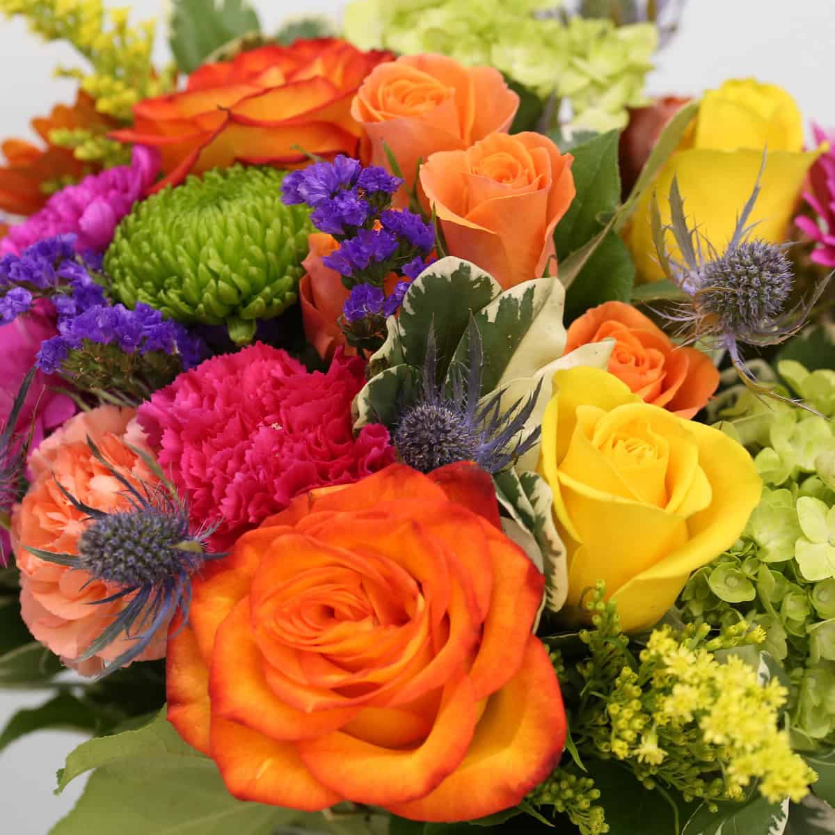 Close-up of Heatwave bouquet featuring orange roses, yellow roses, hydrangea, carnations, statice and blue eryngium flowers.