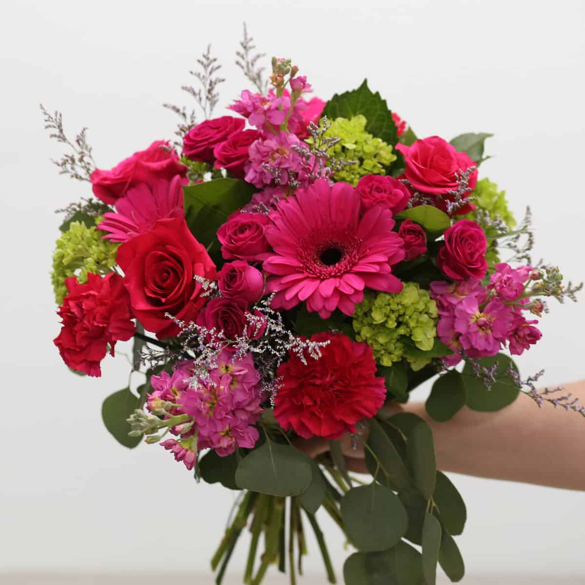 Raspberry Bloom summer bouquet featuring hot pink gerbera daisies, roses, spray roses, hydrangea, carnations, stock and eucalyptus.