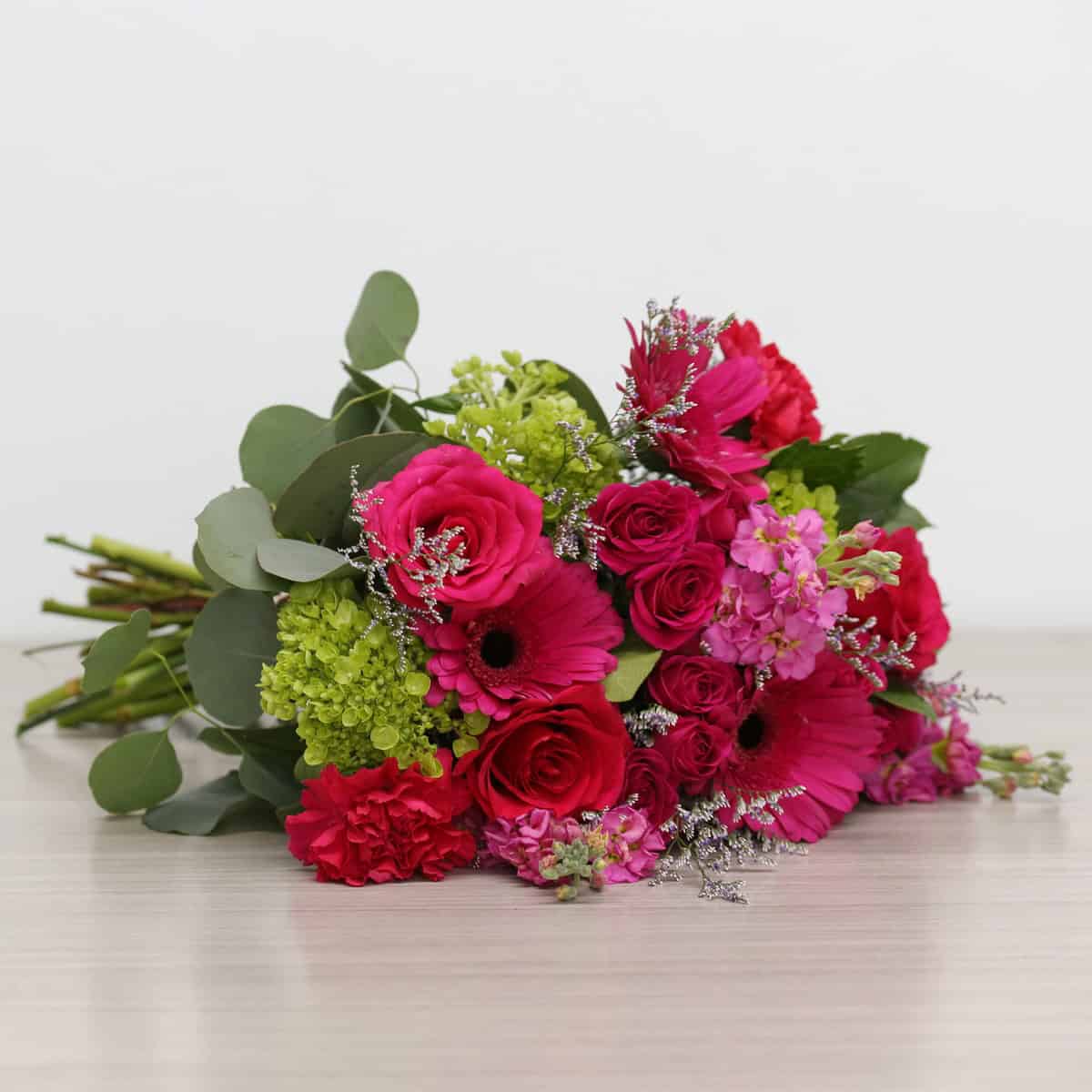 Hand-tied Raspberry Bloom bouquet featuring hot pink gerberas, roses, spray roses, hydrangea, carnations and eucalyptus.