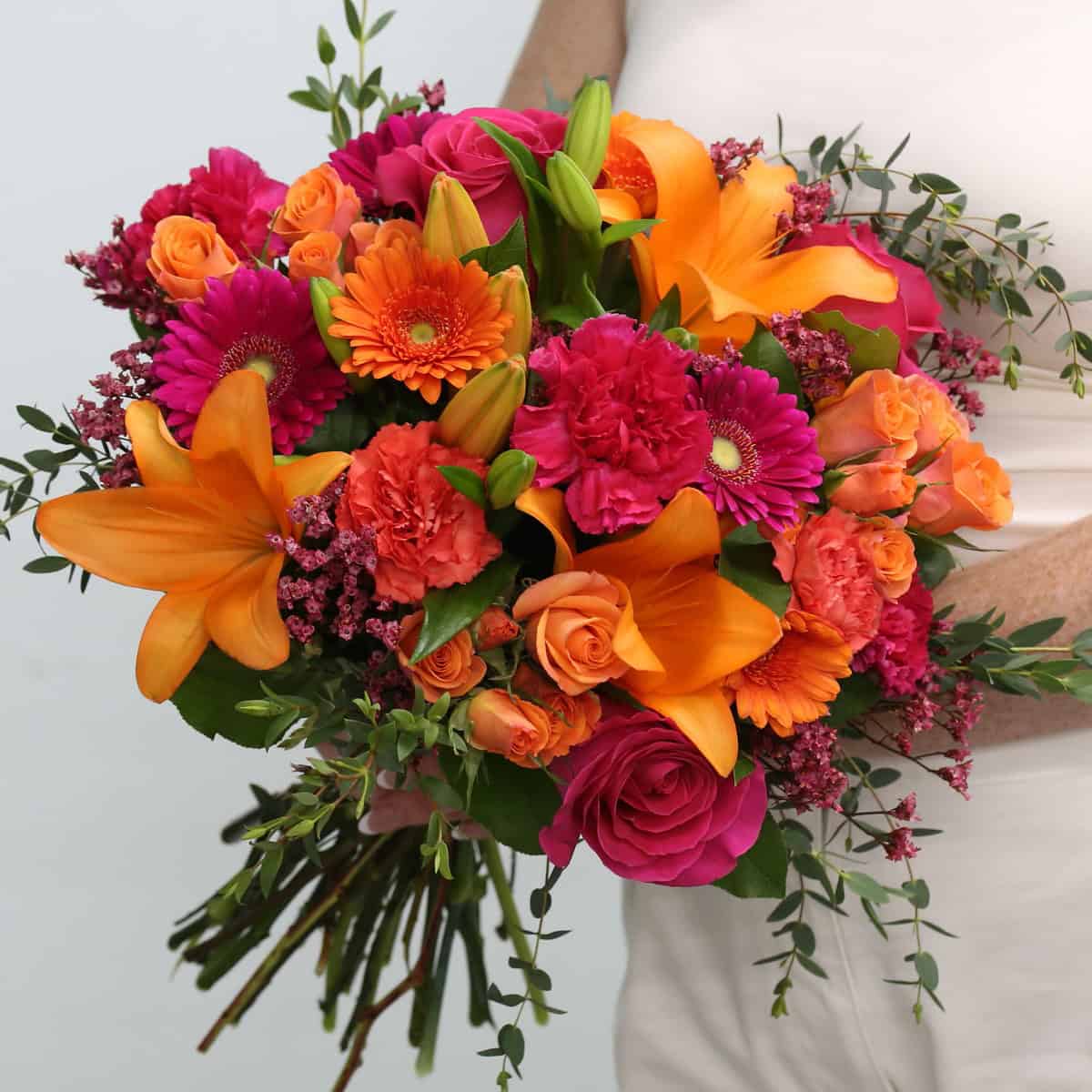 Hand-tied Tropical Sunset bouquet featuring orange lilies, pink roses, gerbera daisies, carnations, and fresh greenery.