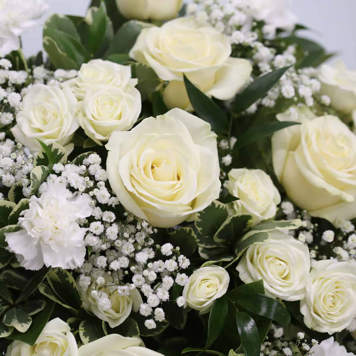 Close-up of the Deepest Sympathy Arrangement featuring white roses, spray roses, carnations, baby's breath and greenery.