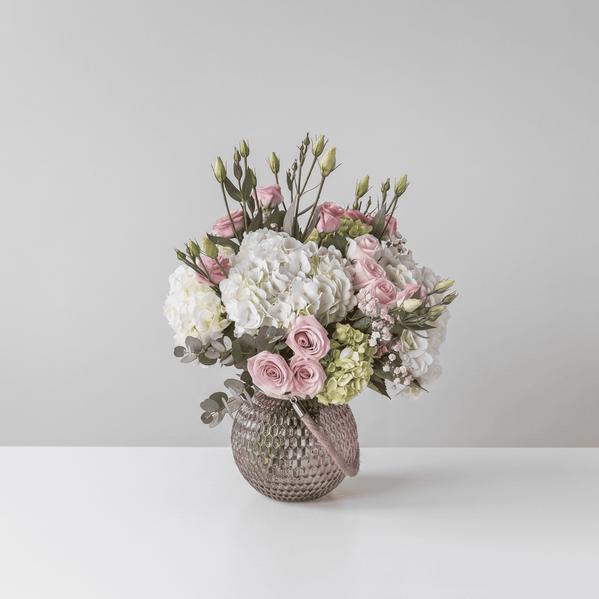 Alexis floral arrangement with blush roses, white hydrangeas, pink lisianthus and eucalyptus in a mauve glass vase