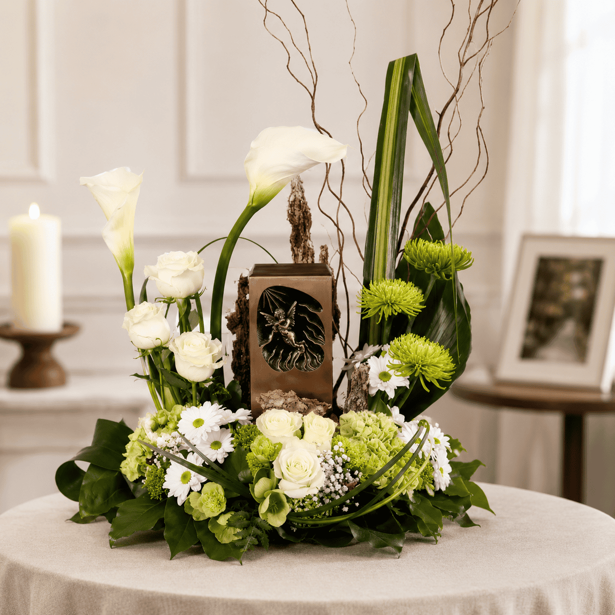 Angel in Heaven Urn Arrangement featuring white calla lilies, white roses, green hydrangeas and white daisies surrounding a decorative urn.