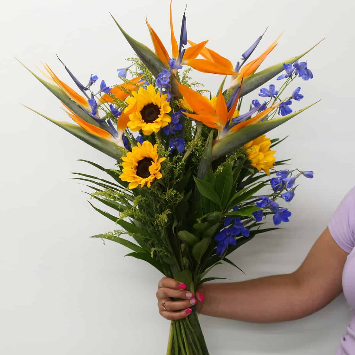 Hand-tied Celeste bouquet with Birds of Paradise, sunflowers, blue delphinium and tropical foliage.