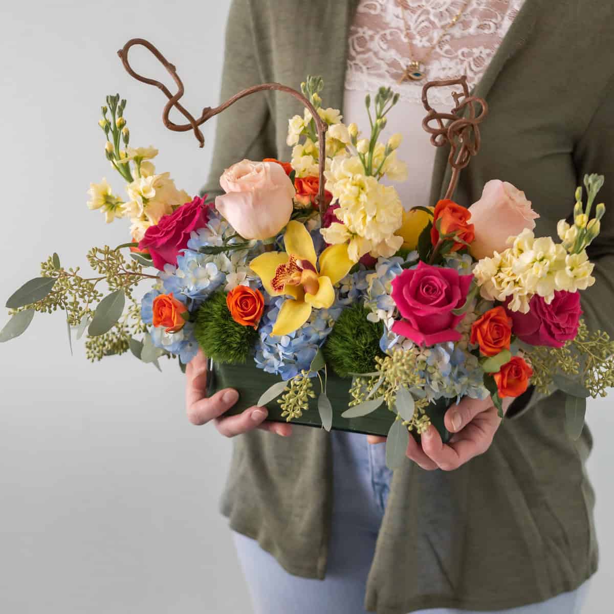 Woman holding the Charming Delight Arrangement with roses, blue hydrangeas and yellow cymbidium orchid