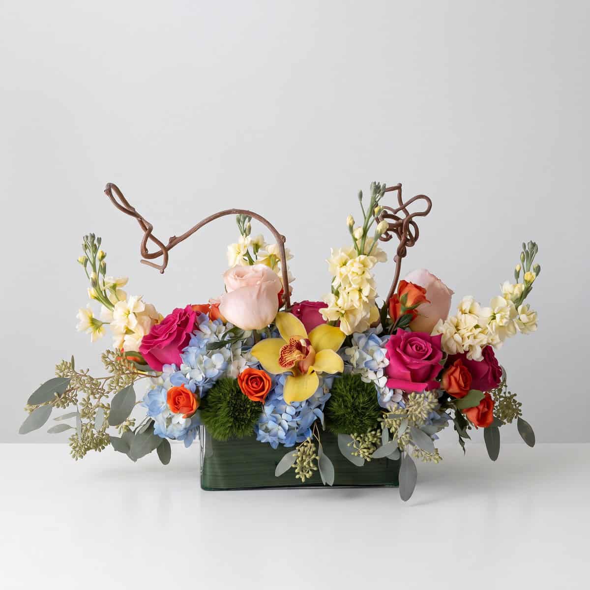 Woman holding the Charming Delight Arrangement with roses, blue hydrangeas and yellow cymbidium orchid