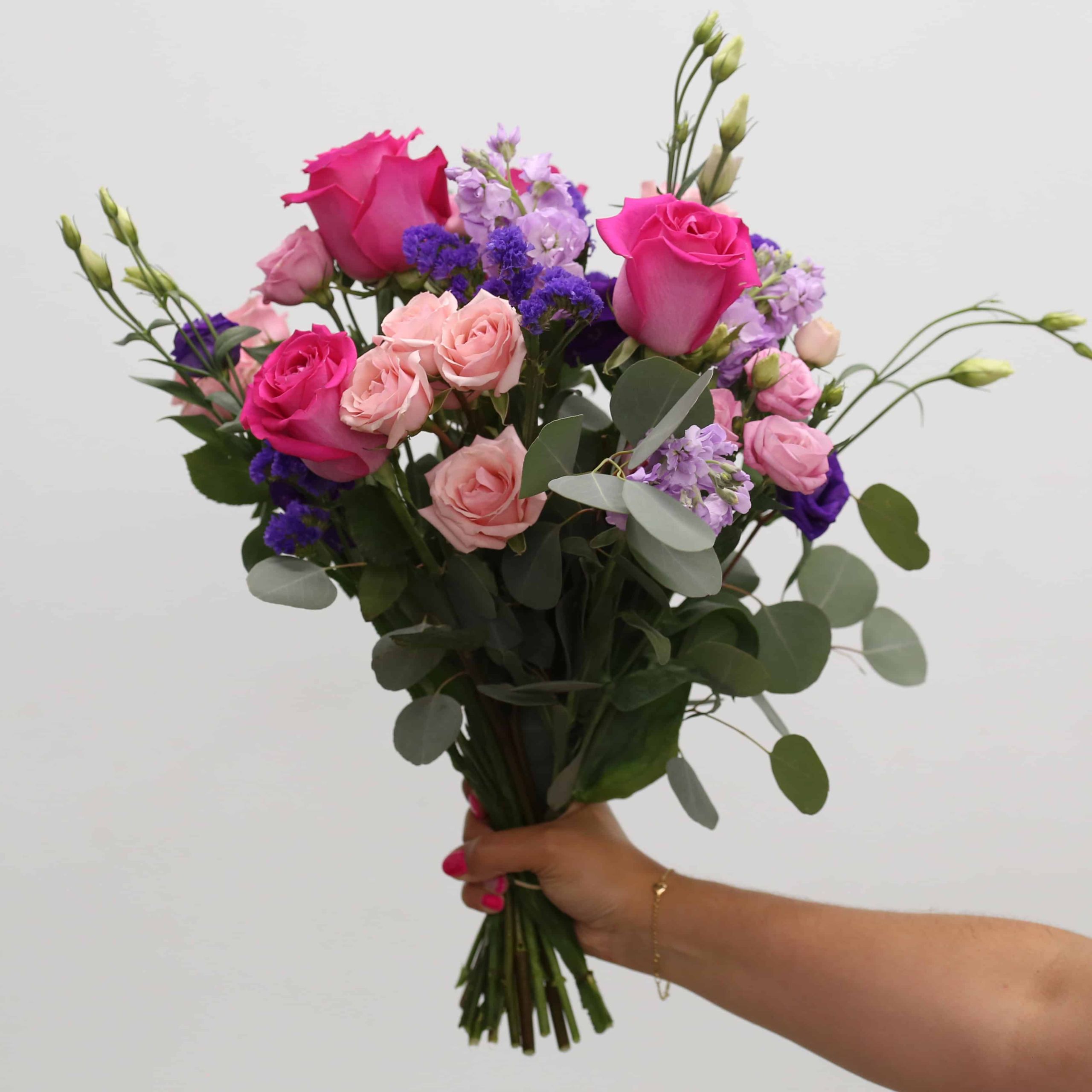 Hand-tied Childlike Wonder bouquet with pink roses, blush spray roses, purple lisianthus and eucalyptus.