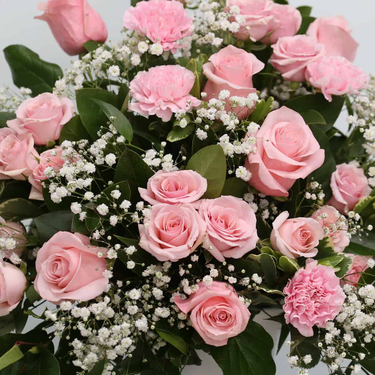 Close-up of the Deepest Sympathy Arrangement featuring pink roses, pink spray roses, carnations, baby's breath and fresh greenery.