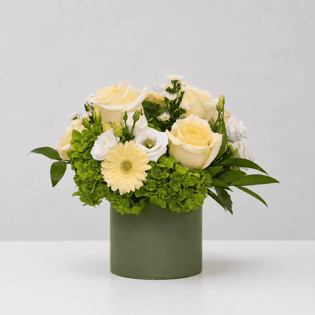 Garden Harmony flower arrangement featuring ivory roses, green hydrangea, white lisianthus and a pale yellow gerbera in a modern green vase.