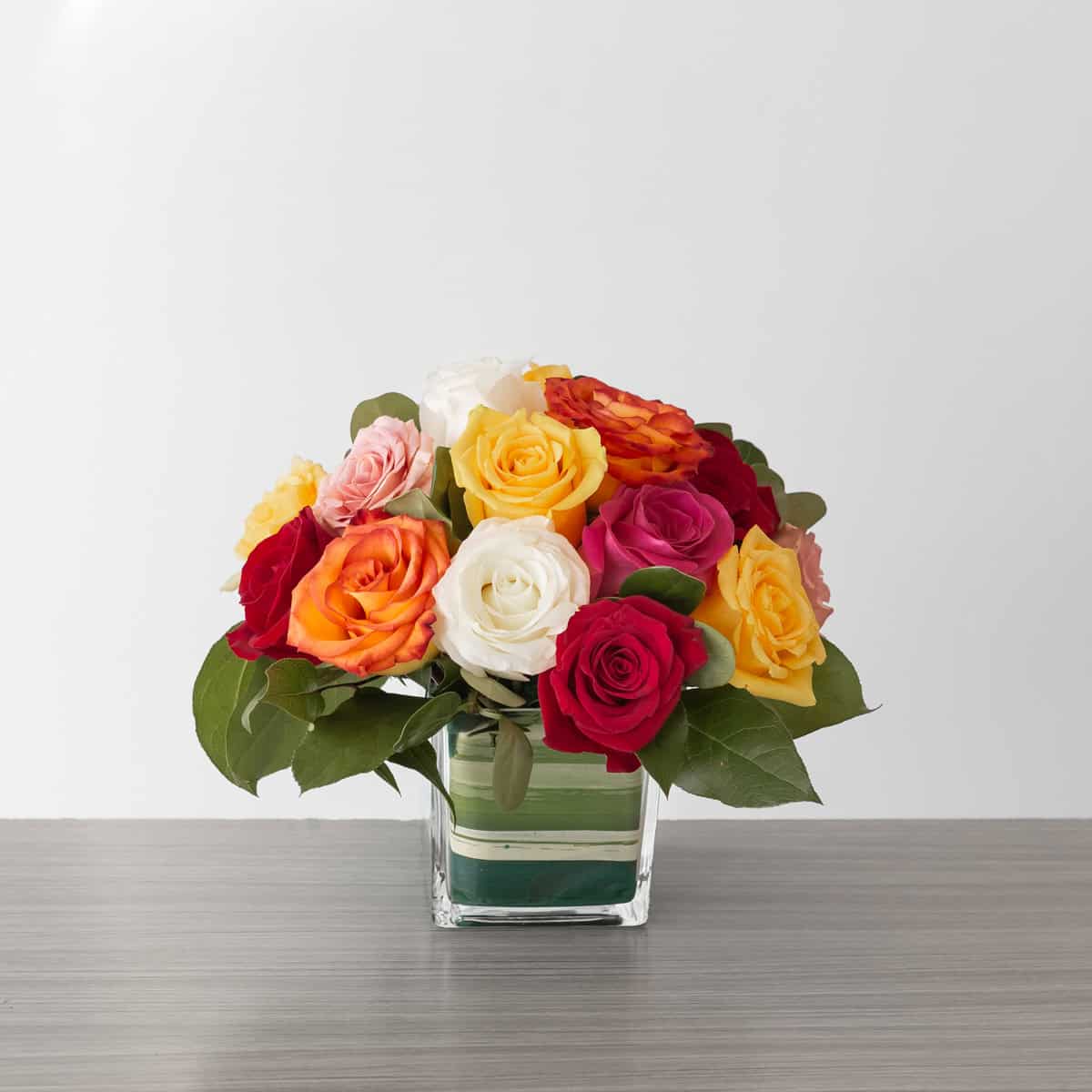 Deluxe Lush Life Roses arrangement with 18 assorted premium roses in a clear glass cube vase.