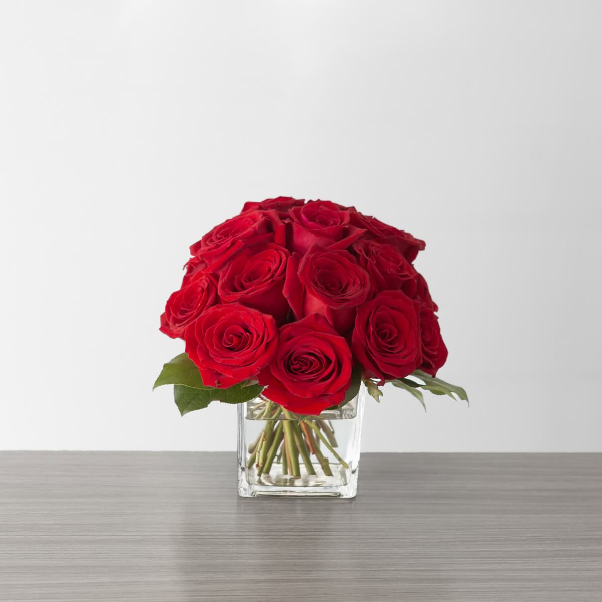 Deluxe Lush Life Roses with 18 premium red roses in a clear glass cube vase.