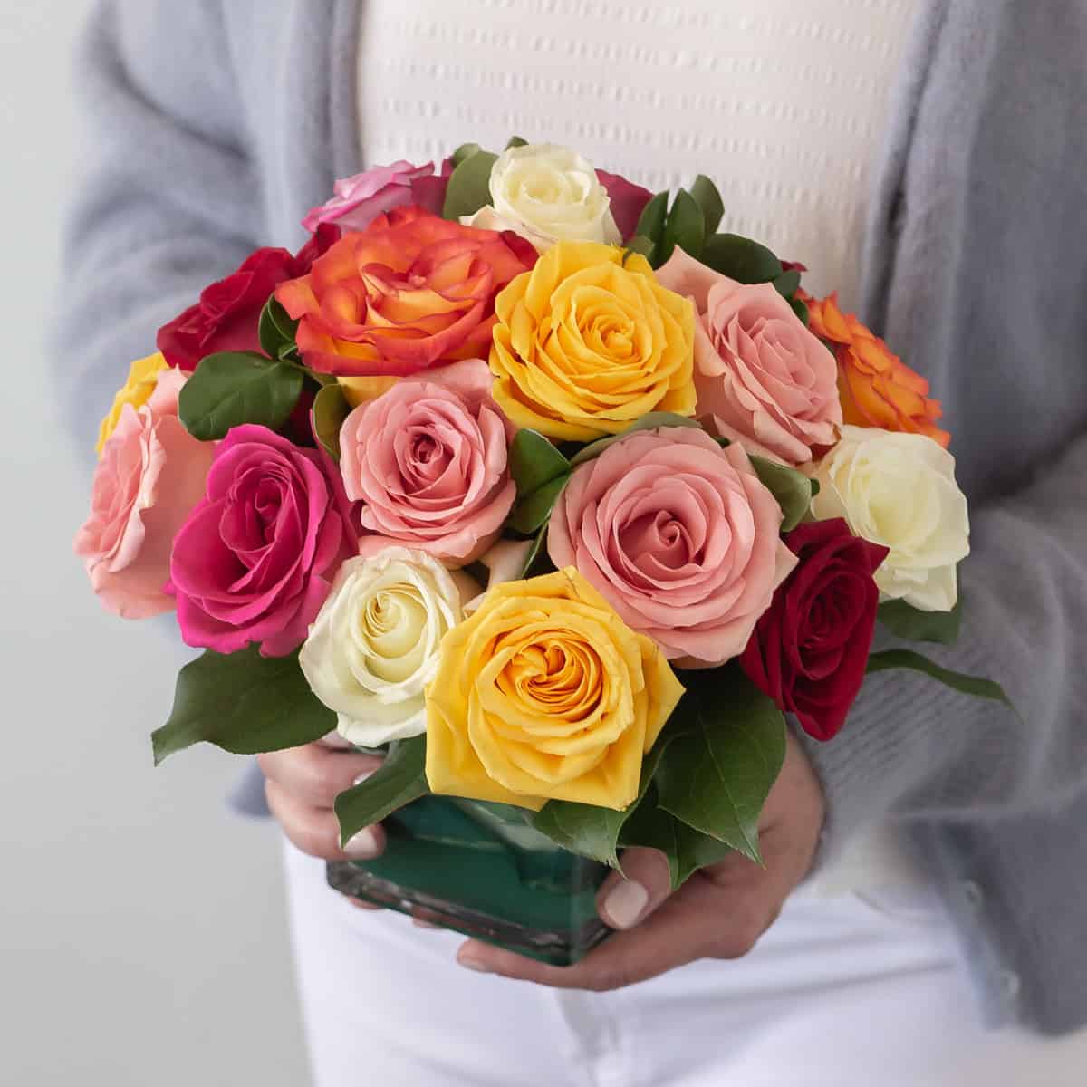 Person holding the premium Lush Life Roses arrangement with 24 assorted roses in a clear glass vase.