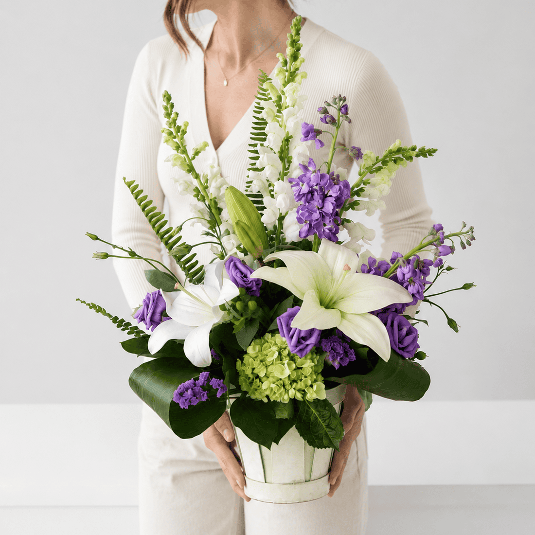 Woman holding the New Beginnings flower arrangement with white lilies, green hydrangea and purple lisianthus.