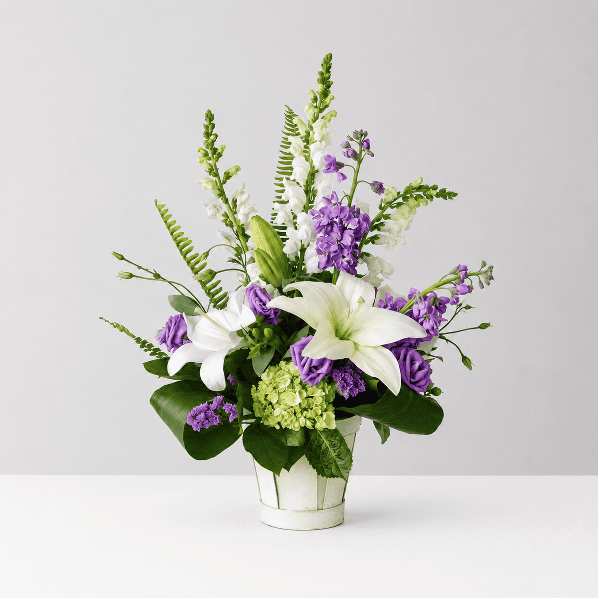 New Beginnings flower arrangement featuring white lilies, green hydrangea, purple lisianthus, white snapdragons and lavender stock.
