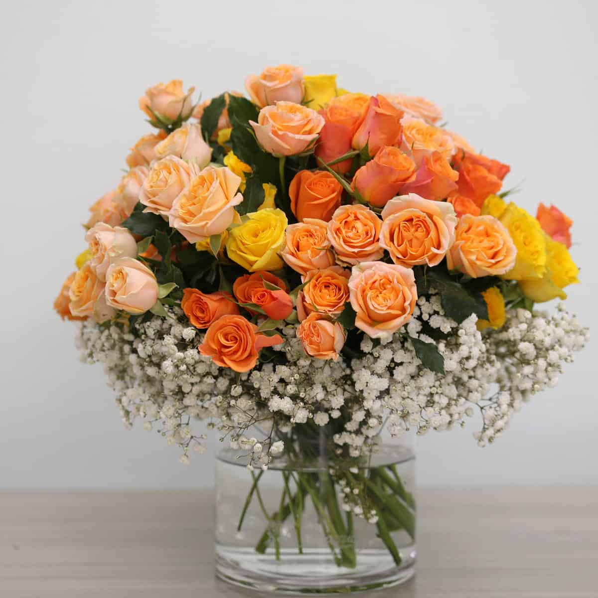 Deluxe Peach Romance spray rose arrangement in a glass vase with peach, orange and yellow blooms and baby's breath.