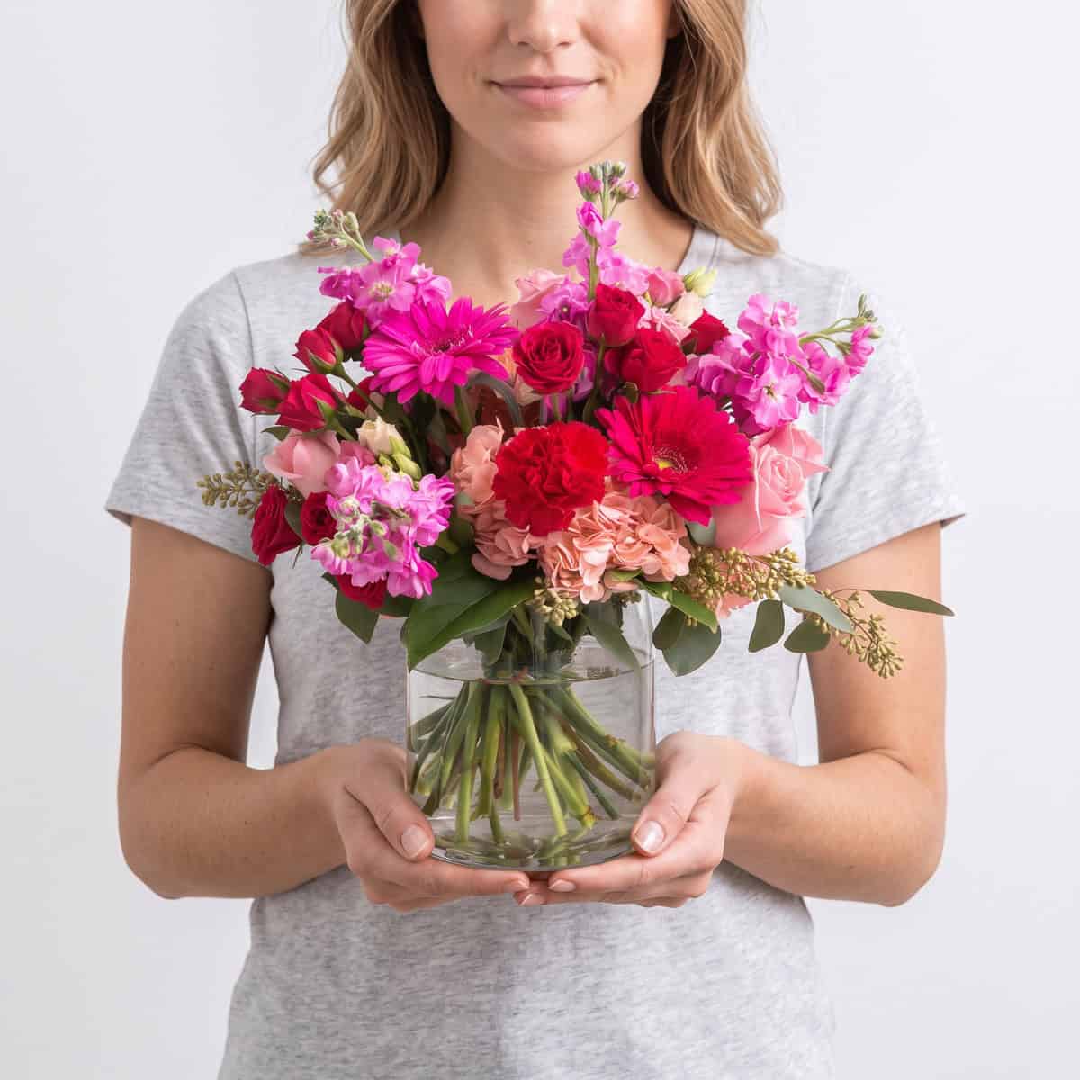 Woman holding the Pink Flamingo flower arrangement in a clear glass vase with vibrant pink flowers.