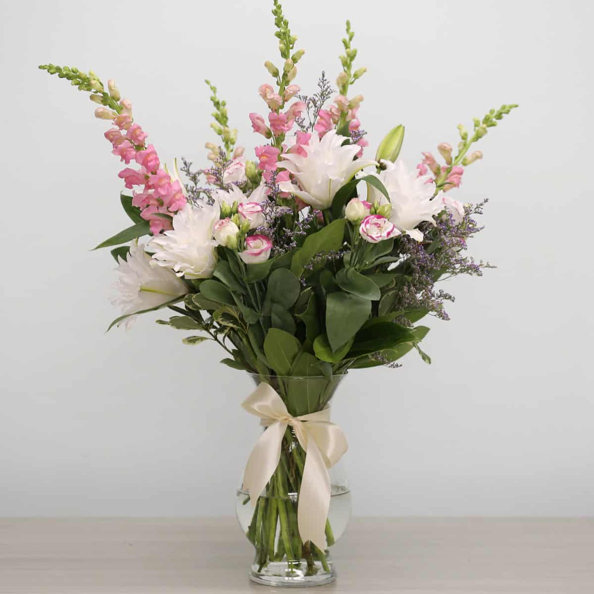 Rosalie floral arrangement in a clear glass vase with fragrant RoseLilies, pink snapdragons, lisianthus and purple caspia.