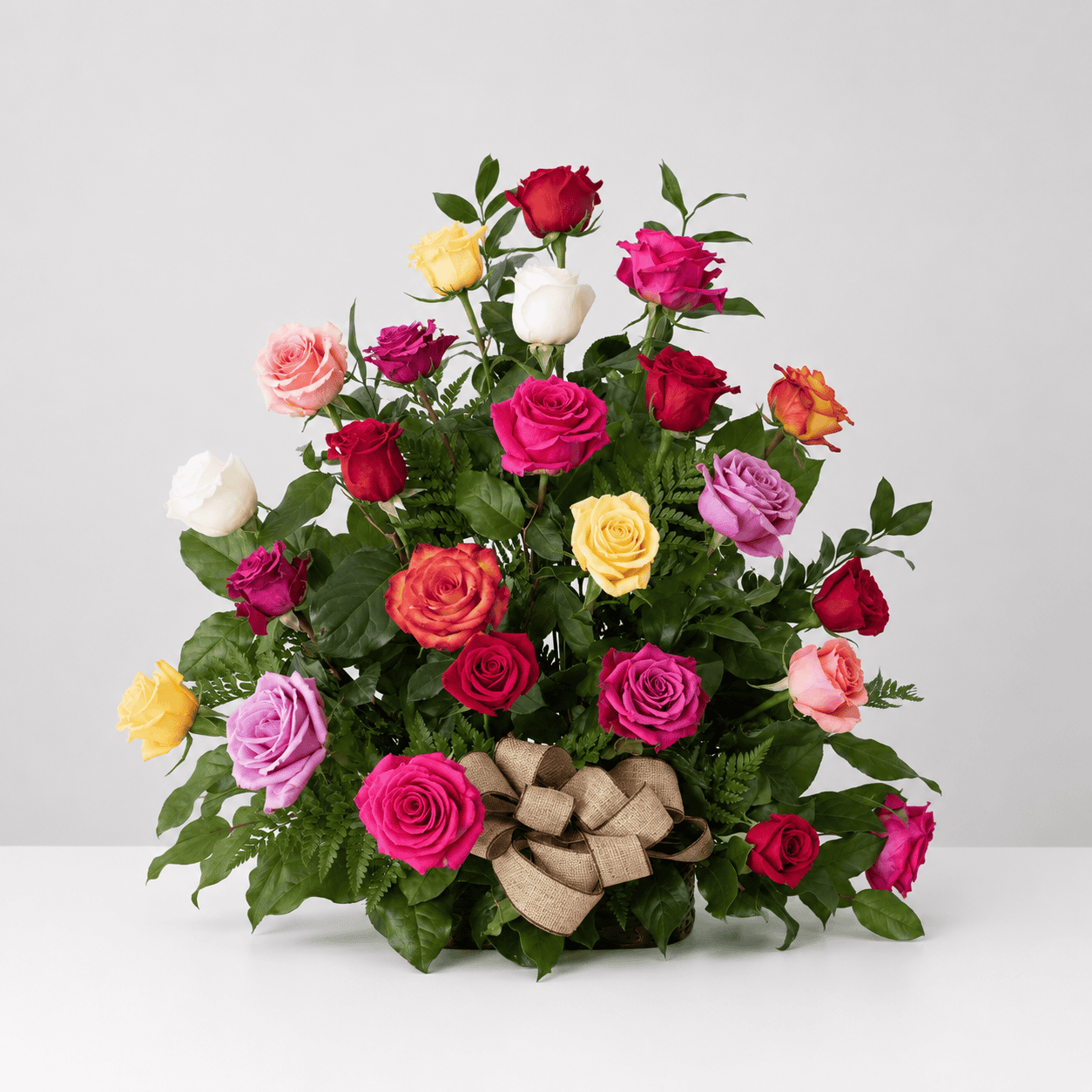 Rose Rush assorted rose arrangement with red, pink, yellow and white roses, lush greenery and a burlap bow.