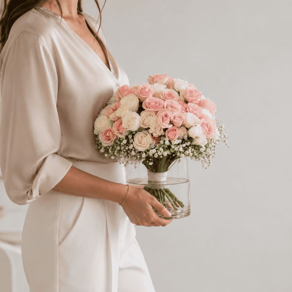 Woman holding the Soft Romance spray rose arrangement with pink and white roses in a modern glass vase.