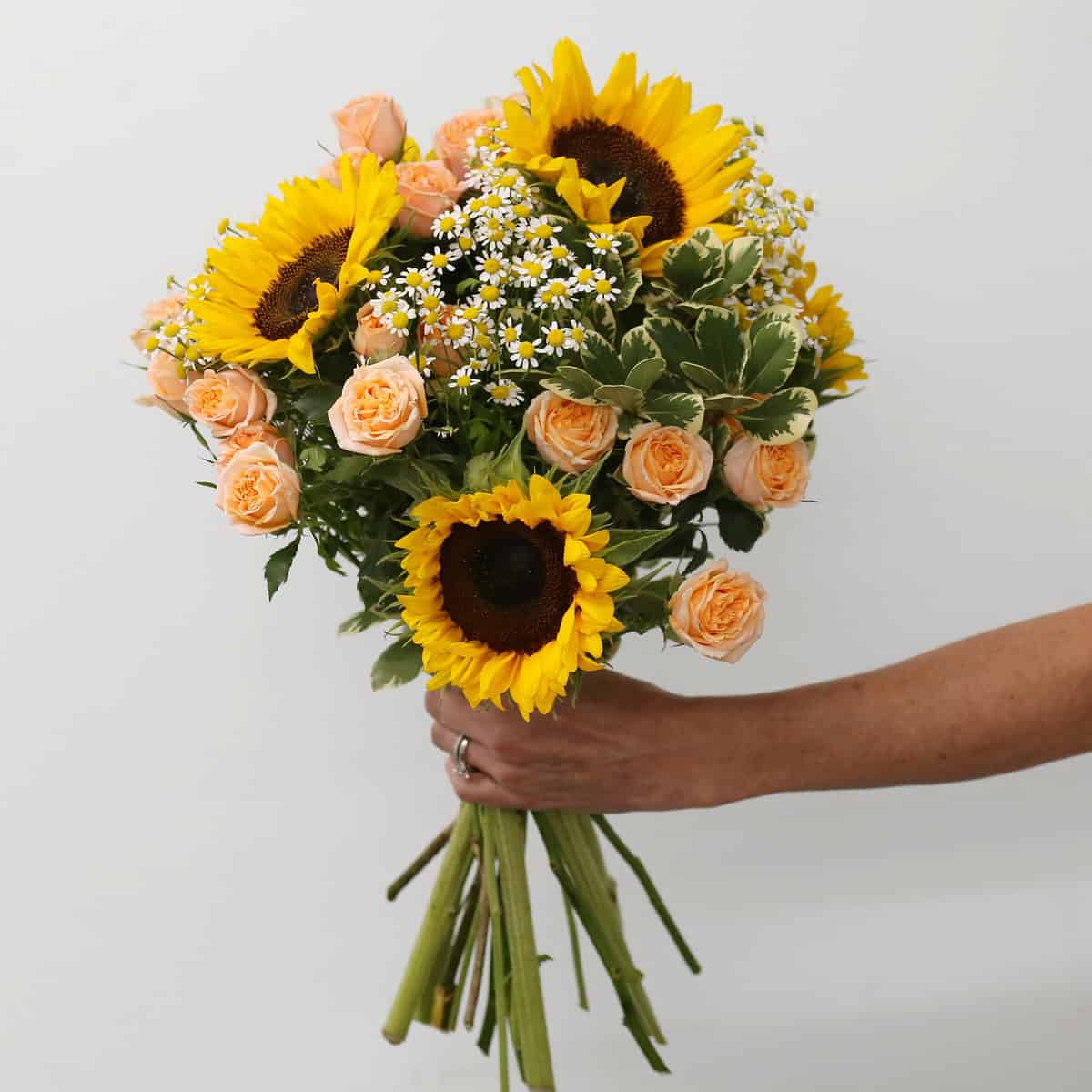 Hand-tied Sunrise Bouquet with fresh sunflowers, peach spray roses, chamomile and variegated pittosporum.