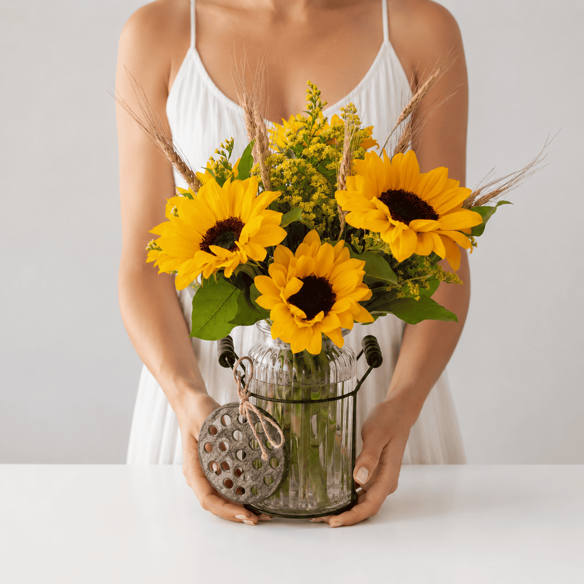 Woman holding the Sunshine Sunflowers arrangement in a rustic glass vase.