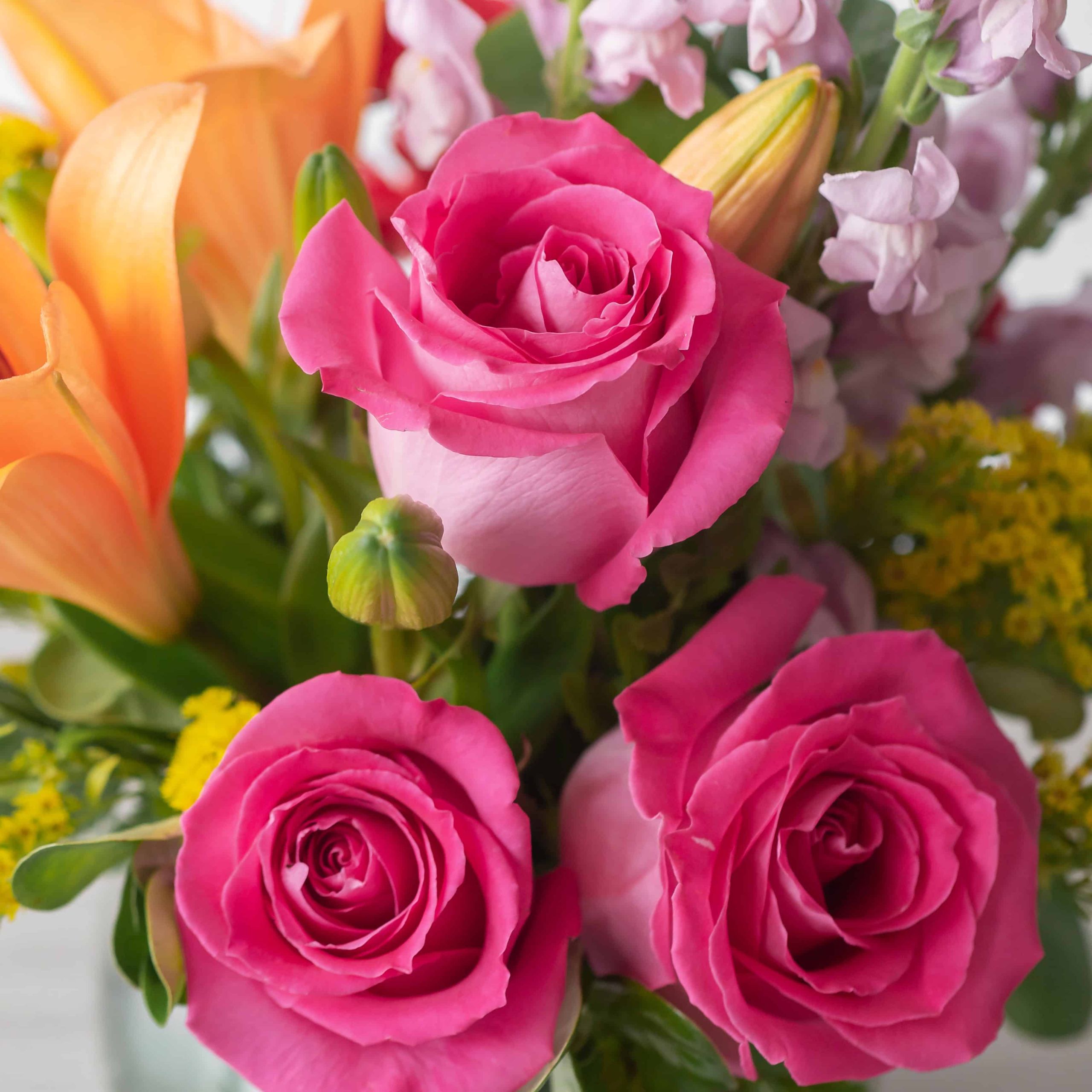 Close-up of vibrant hot pink roses with orange lilies and seasonal flowers in the Warmer Days arrangement.