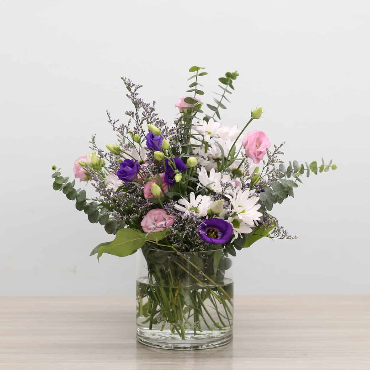 Ariana Deluxe Bouquet arranged in a glass vase with pink and purple lisianthus, white daisies, caspia and eucalyptus