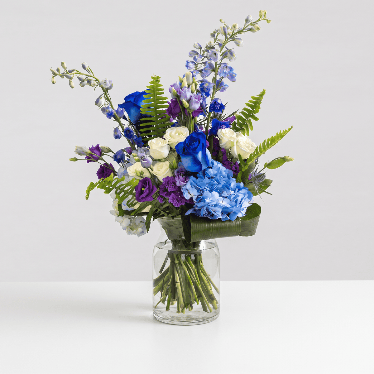 Blue Skies flower arrangement with blue hydrangea, blue and white roses, delphinium and lisianthus in a clear glass vase.