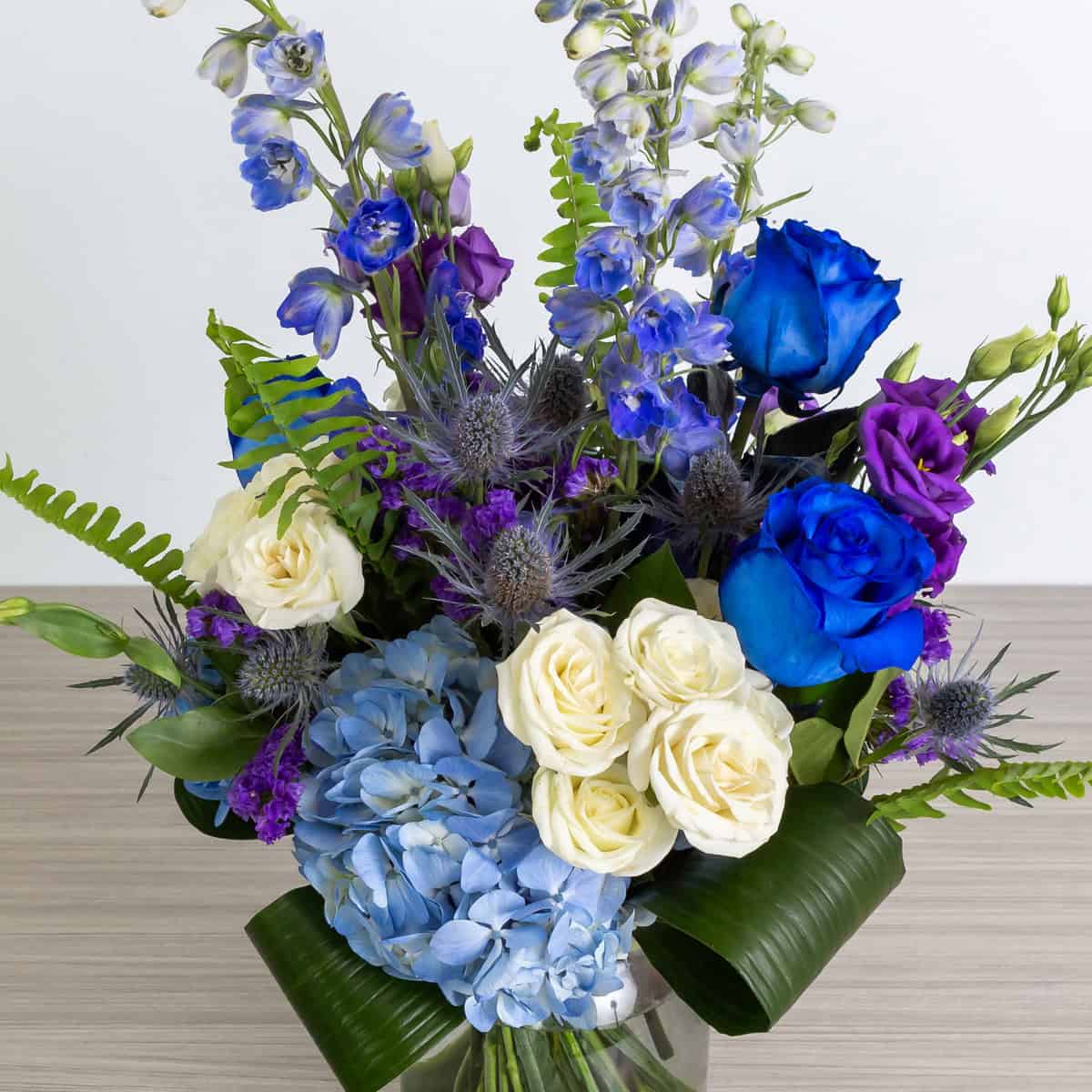 Close-up of Blue Skies arrangement featuring blue hydrangea, blue roses, white roses and purple lisianthus.