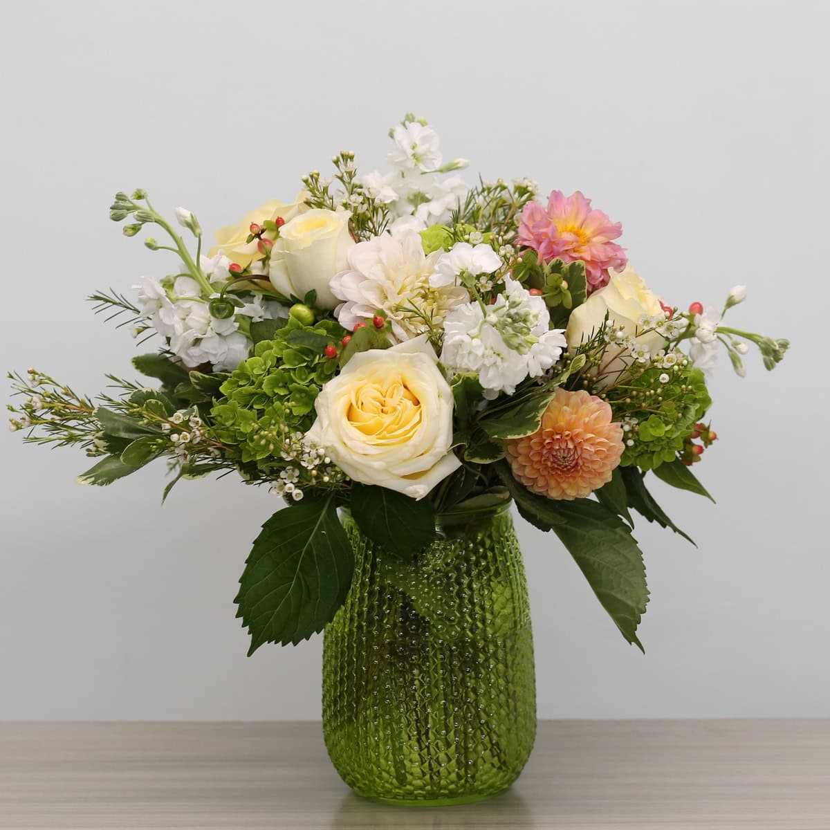 Floral Rhapsody cream and peach flower arrangement with roses, dahlias, green hydrangea and white stock in a green glass vase