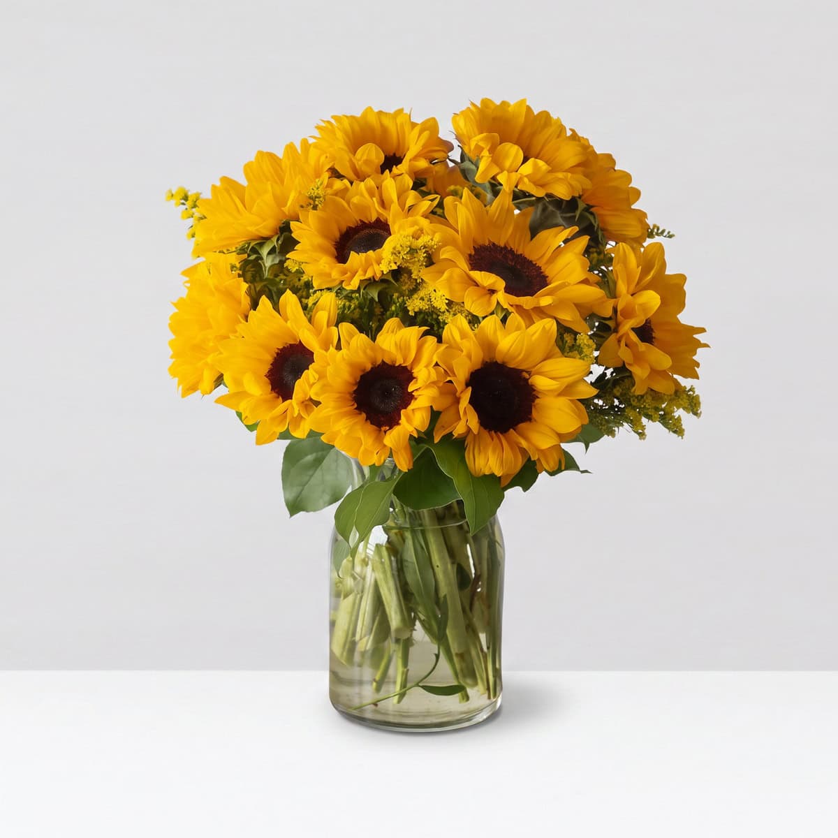 Fresh-cut sunflower bouquet arranged in a clear glass vase with solidago and seasonal greenery.