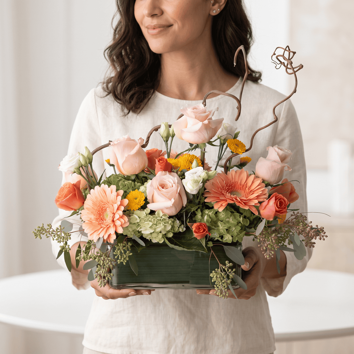 Woman holding the Graceful Elegance flower arrangement with peach roses and decorative curly willow branches.