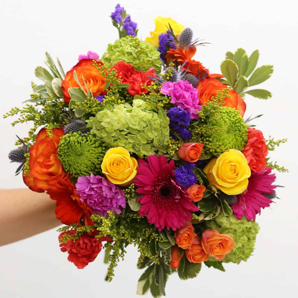 Premium Heatwave hand-tied bouquet with orange and yellow roses, green hydrangea, gerbera daisies, carnations and blue thistle