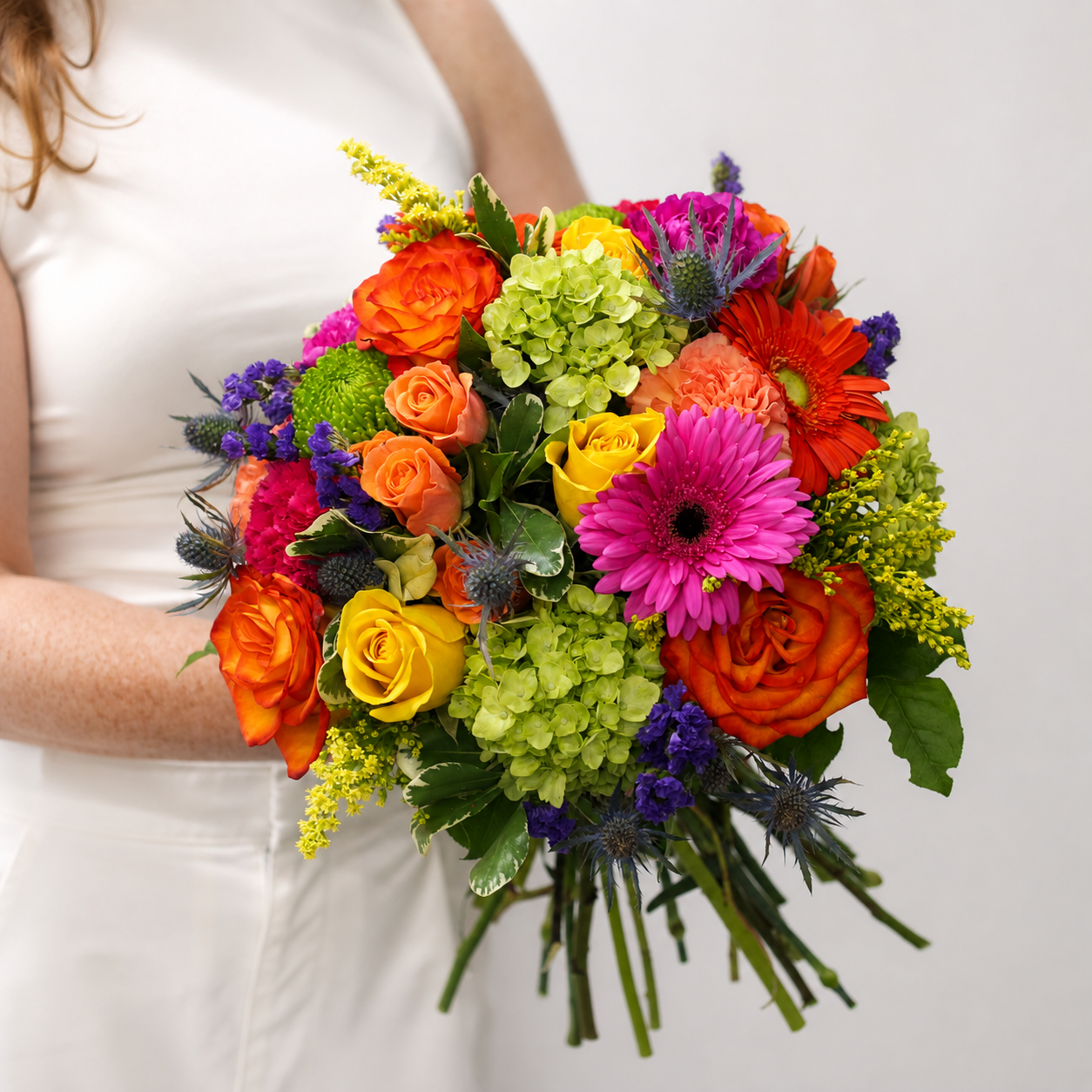 Woman holding the Heatwave summer bouquet with colourful roses, gerbera daisies, green hydrangea, statice and blue thistle.