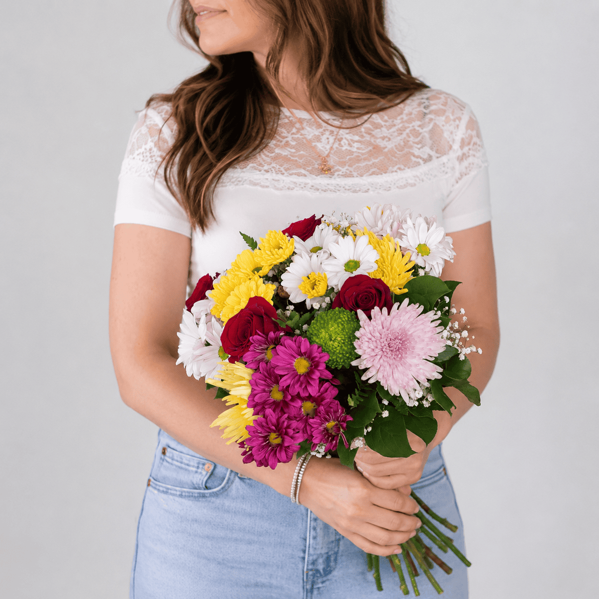 Woman holding the Deluxe Hollandia Daisy Bouquet with red roses, colourful daisies, Fuji chrysanthemums and baby's breath.