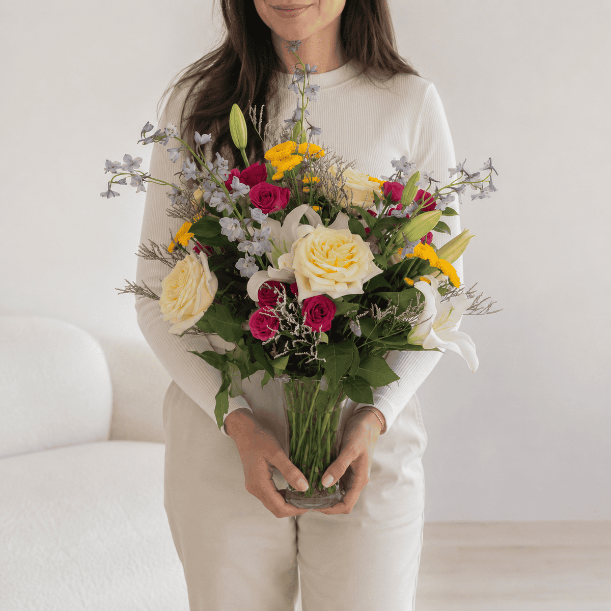 Woman holding the colourful New Day Dawns flower arrangement in a clear glass vase