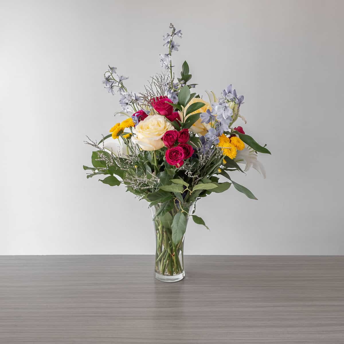 New Day Dawns flower arrangement with cream roses, fuchsia spray roses, white lilies and blue delphinium