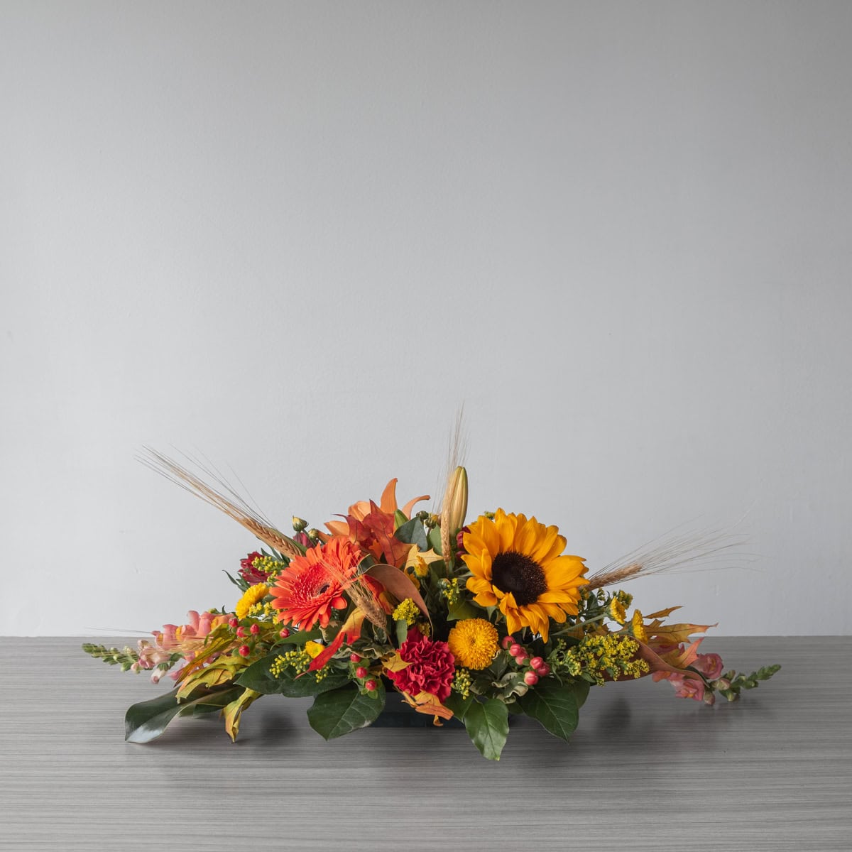 Oval Centerpiece Deluxe with sunflowers, gerbera daisies, carnations, roses and fall flowers in red, yellow and orange