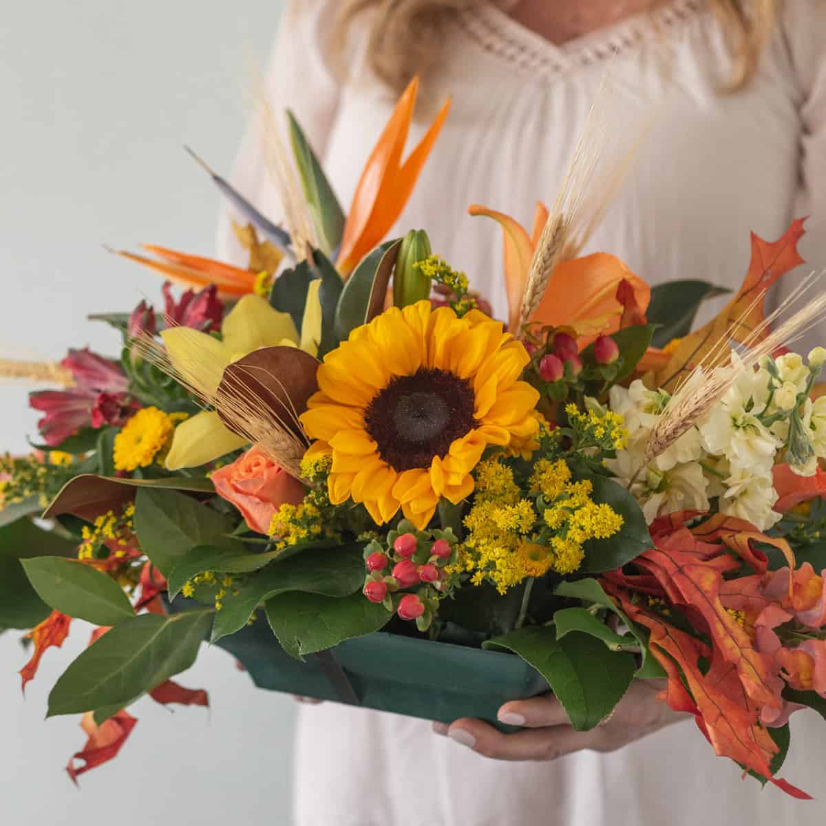 Person holding Premium Oval Centerpiece with sunflowers, roses, orchids, seasonal flowers and fall foliage