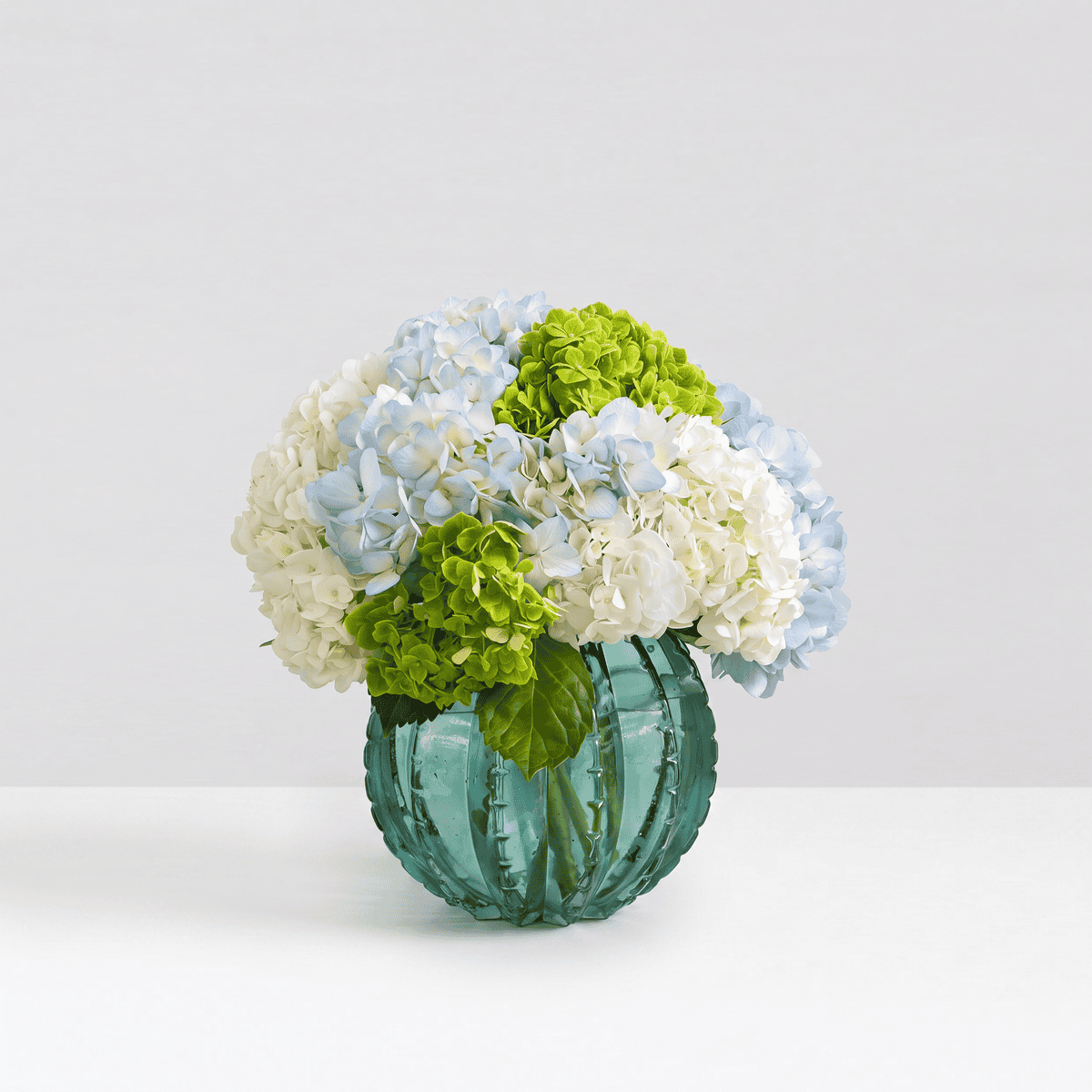 Peridot hydrangea arrangement featuring premium blue, white and green hydrangeas in a textured emerald green glass vase.