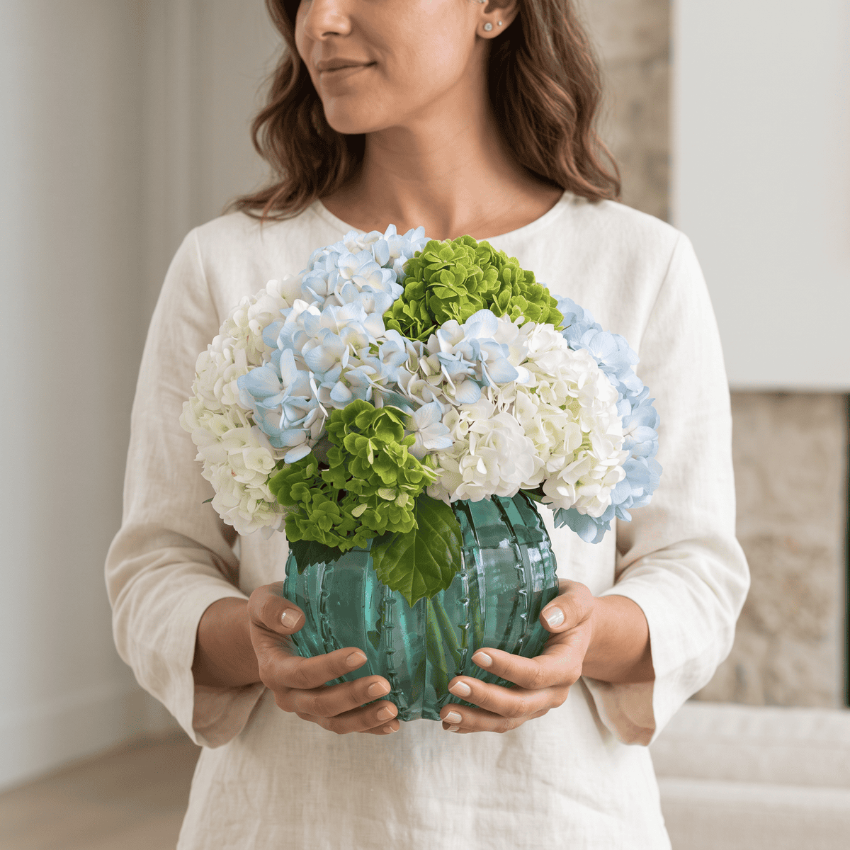 Woman holding the Peridot hydrangea arrangement with blue, white and green hydrangeas in an emerald green glass vase.