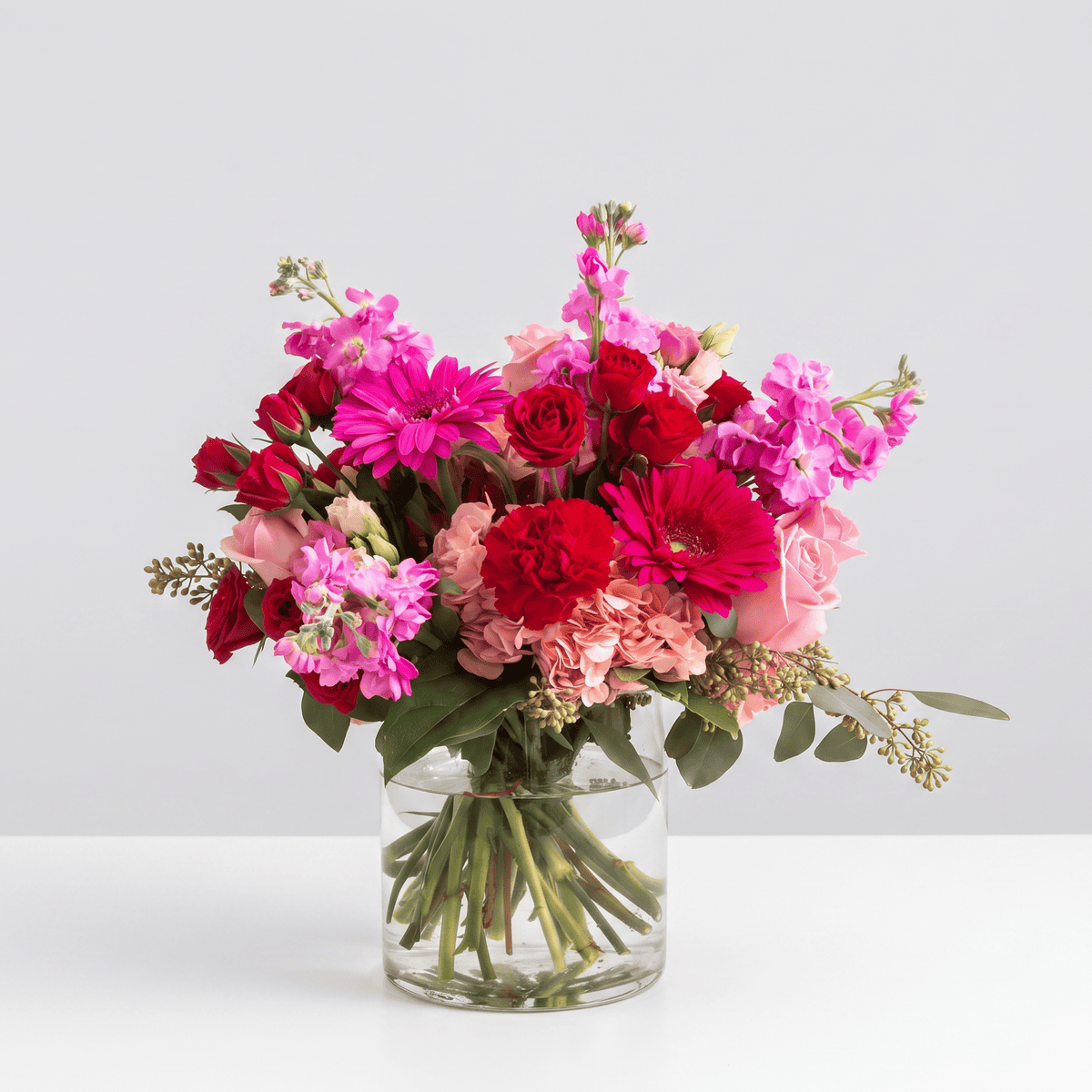 Pink Flamingo flower arrangement featuring pink roses, spray roses, gerbera daisies, hydrangea, double stock and eucalyptus in a clear glass vase.