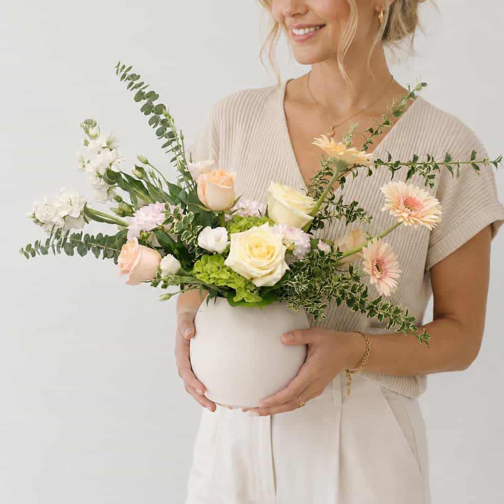 Woman holding Posy Peach garden-style flower arrangement with peach roses, gerbera daisies, hydrangea and greenery